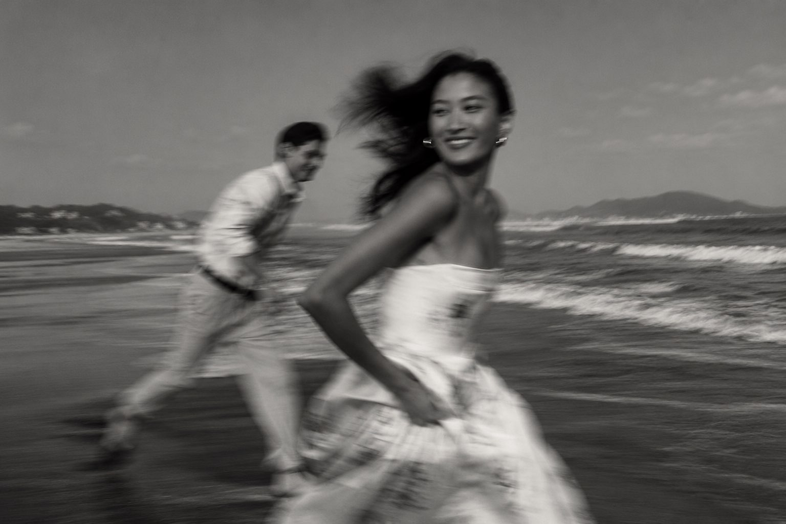 A couple running along a beach, the woman smiling back over her shoulder