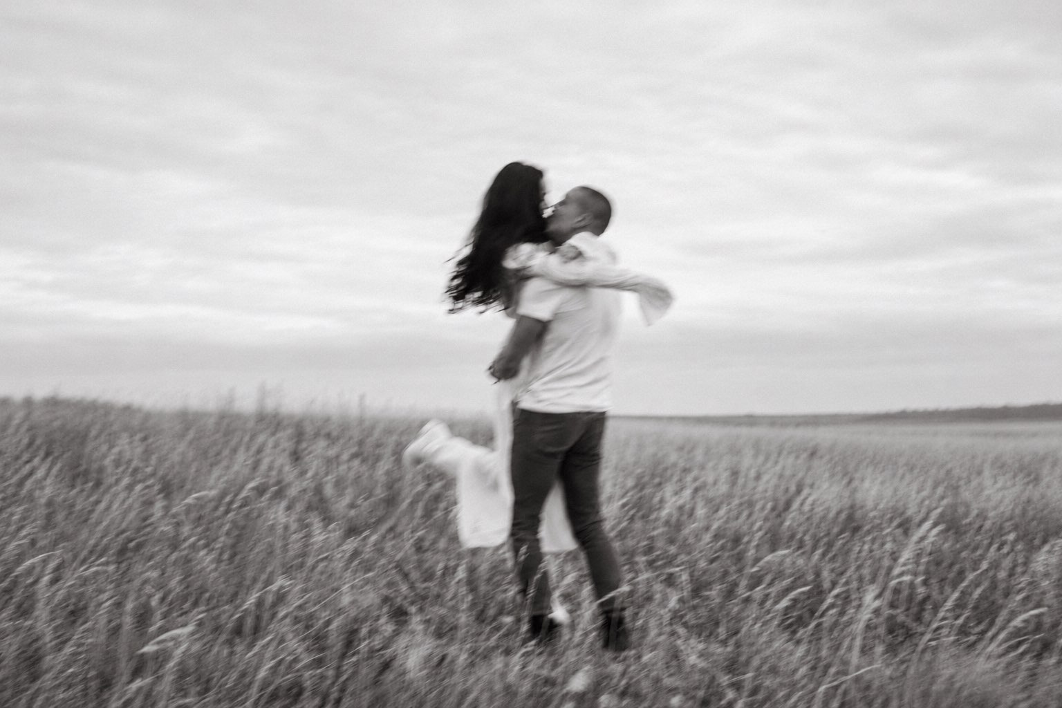 A couple embracing in a windswept field of long grass