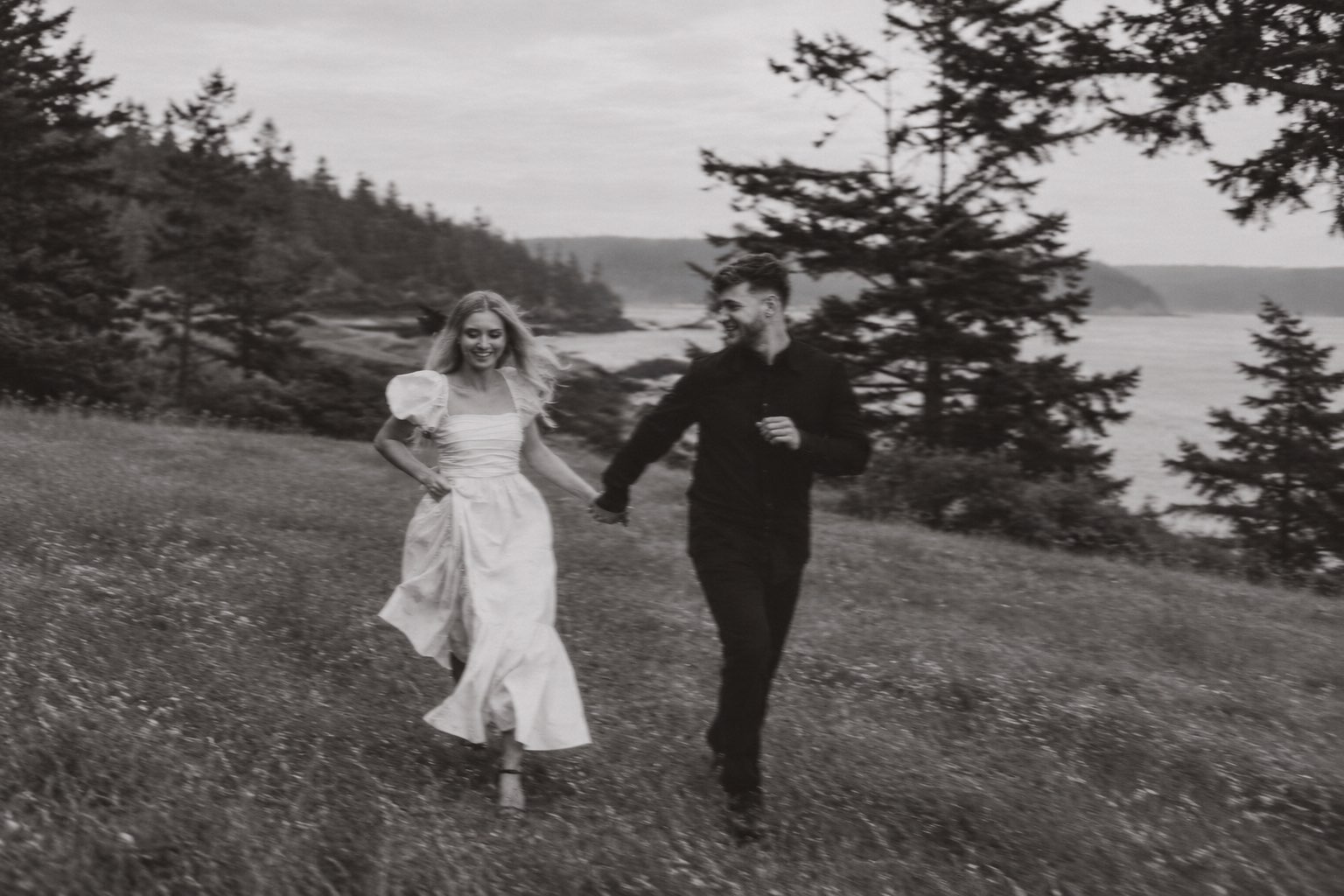 A couple running hand in hand through a hillside meadow above the sea